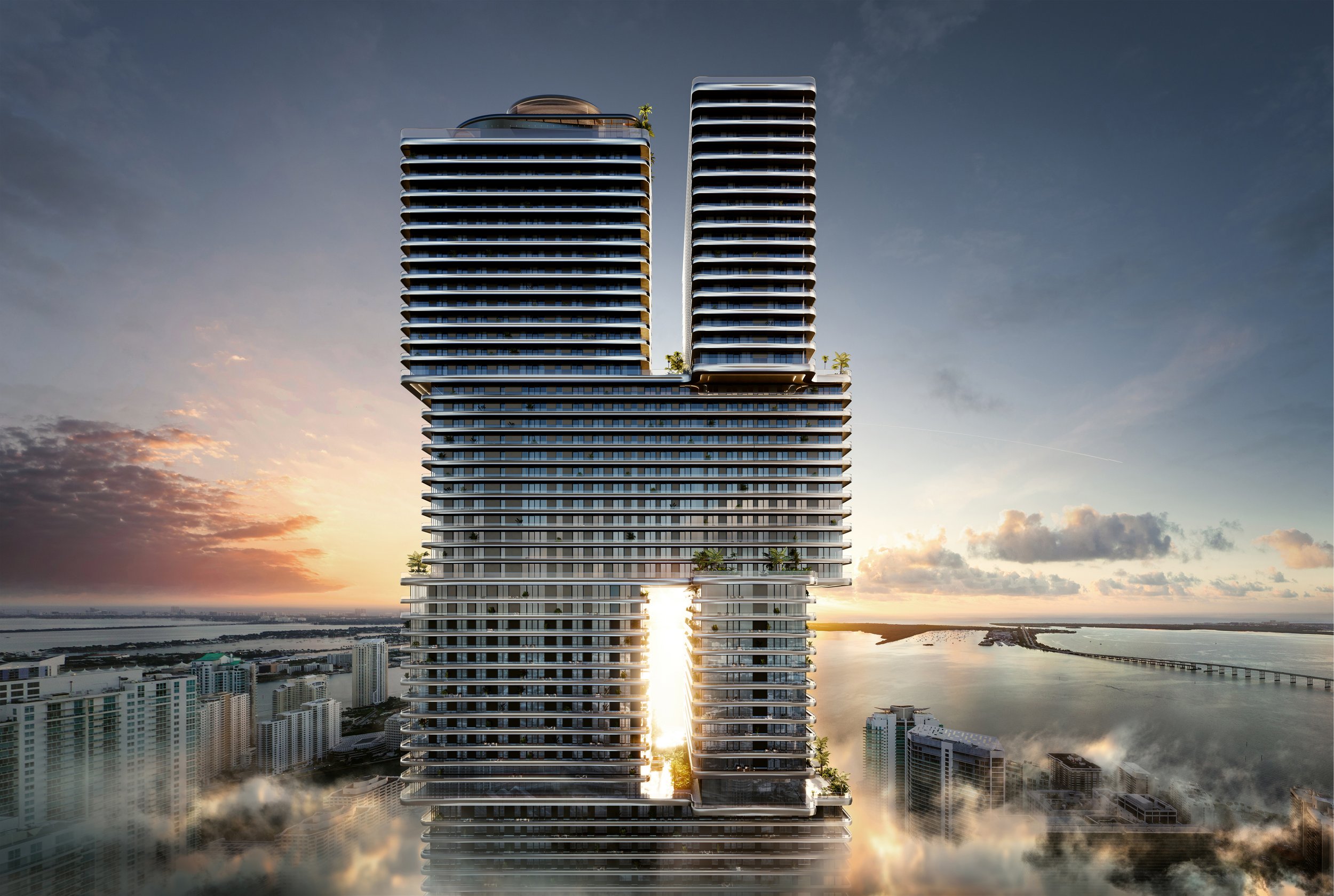 Modern high-rise building with an open center, overlooking a city and water at sunset